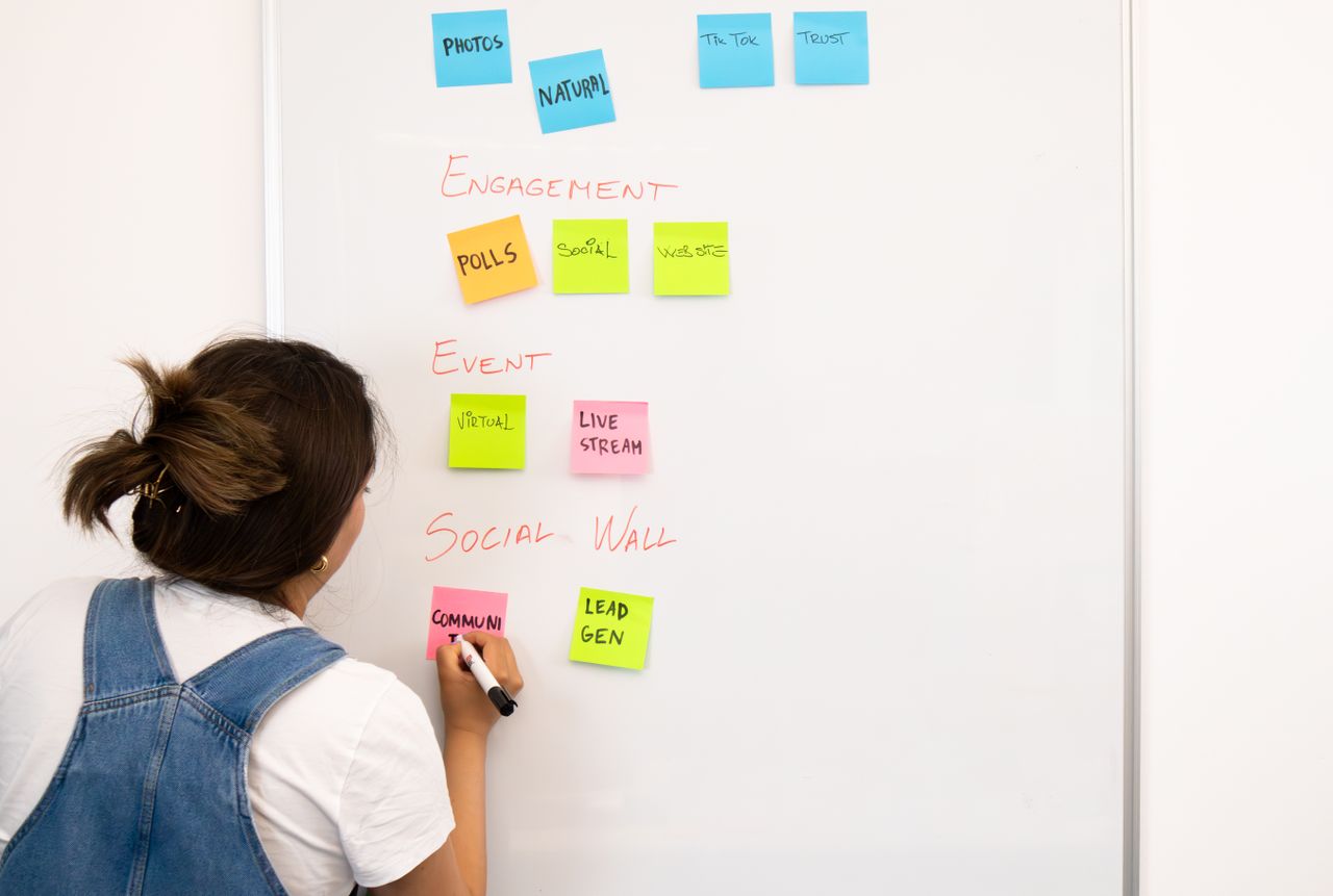services-01 A woman organizing notes on a whiteboard with colorful sticky notes in an office setting.